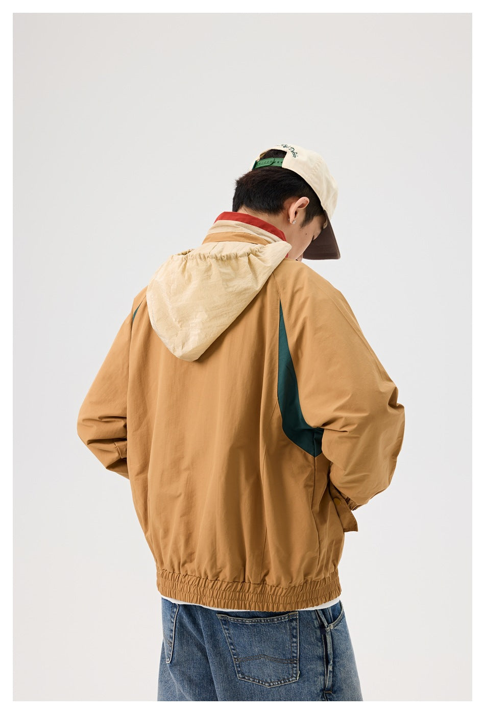 Back view of a model wearing a tan jacket with a light beige hood and dark teal side panels.