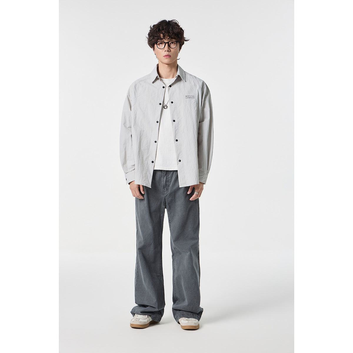Model wearing a light gray button-up shirt with dark buttons and small chest lettering, paired with gray wide-leg jeans.