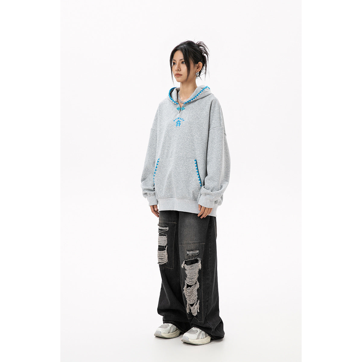 Full-length view of a model wearing an oversized gray hoodie with blue trim and black distressed wide-leg jeans.