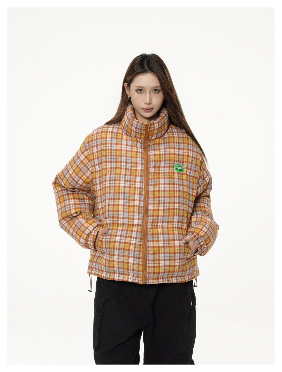 Model wearing the orange plaid puffer-style jacket zipped up with hands in pockets, paired with black cargo pants