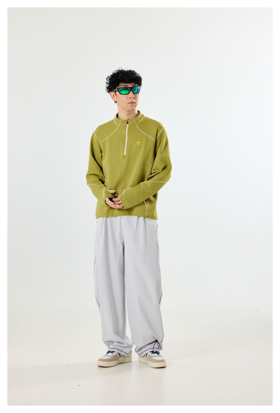 Model wearing an olive quarter-zip pullover with light contrast seams and loose light-gray trousers.