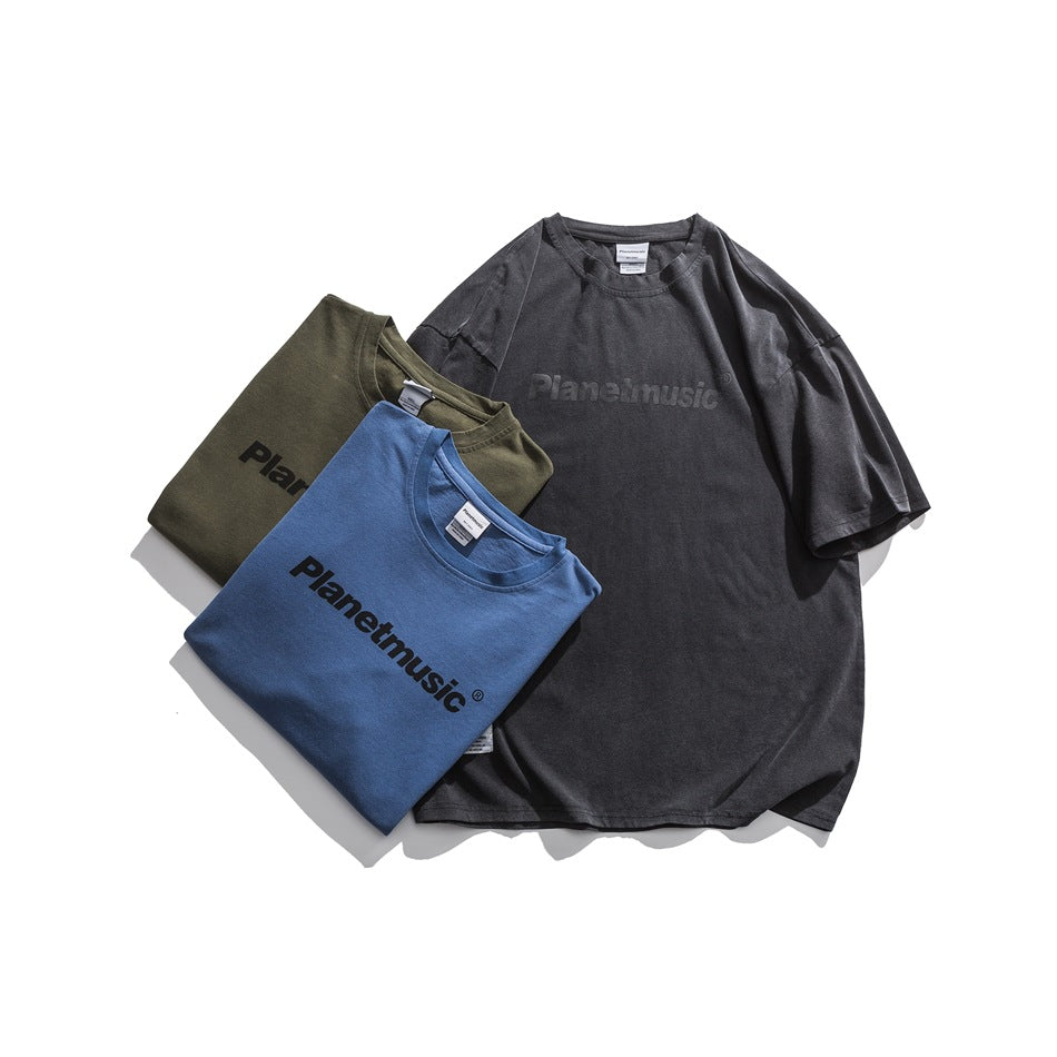 Gray T-shirt laid flat with folded blue and army green T-shirts, all with chest lettering prints