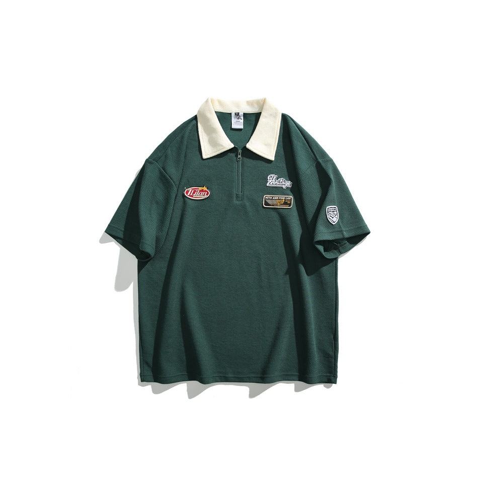 Dark green waffle-knit short-sleeve polo with cream collar, quarter zipper and chest patches, flat front view