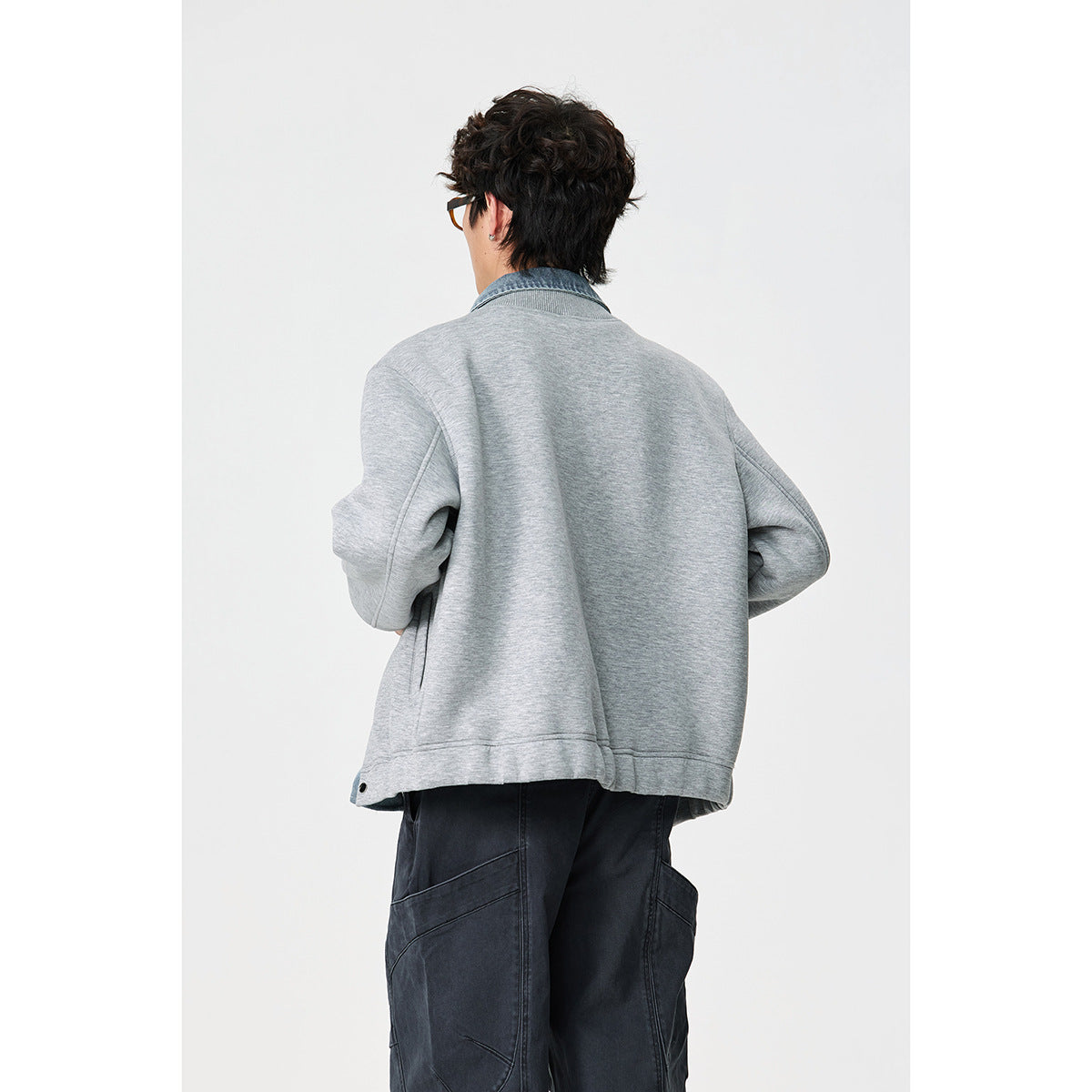Back view of a model wearing a light gray jacket with a blue denim collar and dark cargo pants.