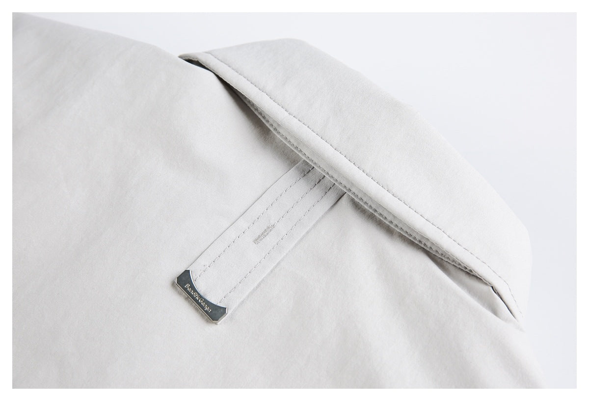 Close-up of a pale gray garment collar with a small metal tag and stitched collar stand.
