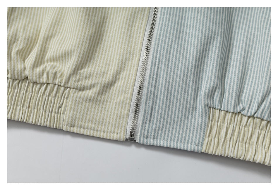 Close-up of a silver front zipper between cream and blue-gray striped panels, with an elasticized hem.