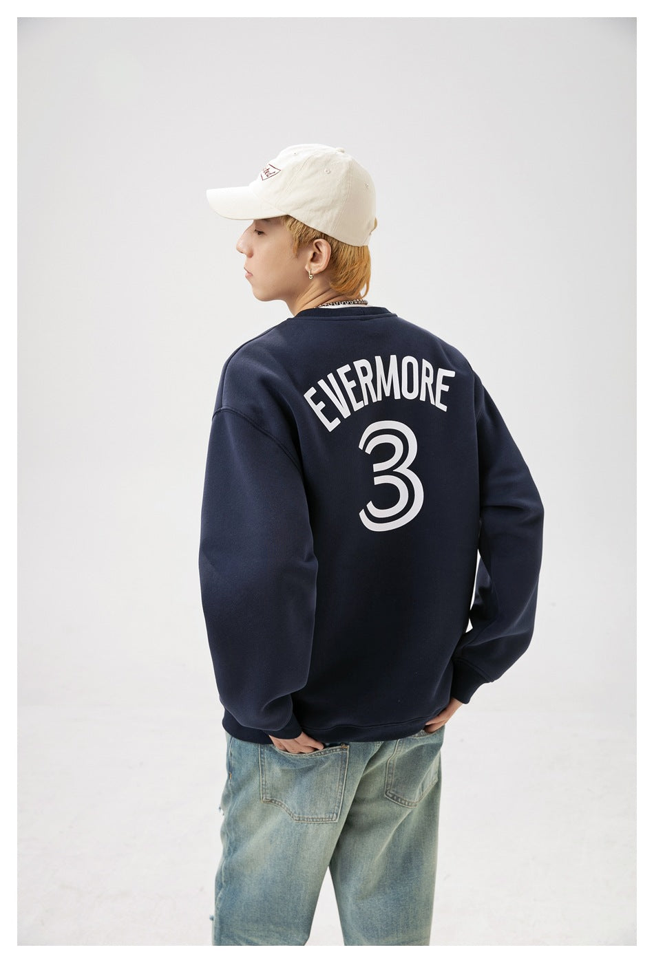 Model showing the back of a navy sweatshirt with white arched lettering and a large number 3.