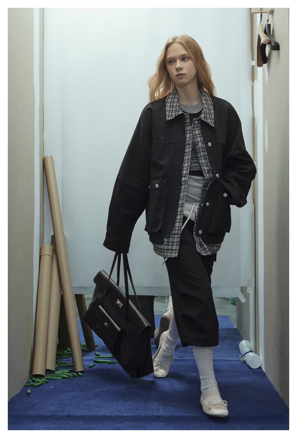 Model wearing an oversized black jacket with silver buttons and plaid collar over a gray top and loose black cropped