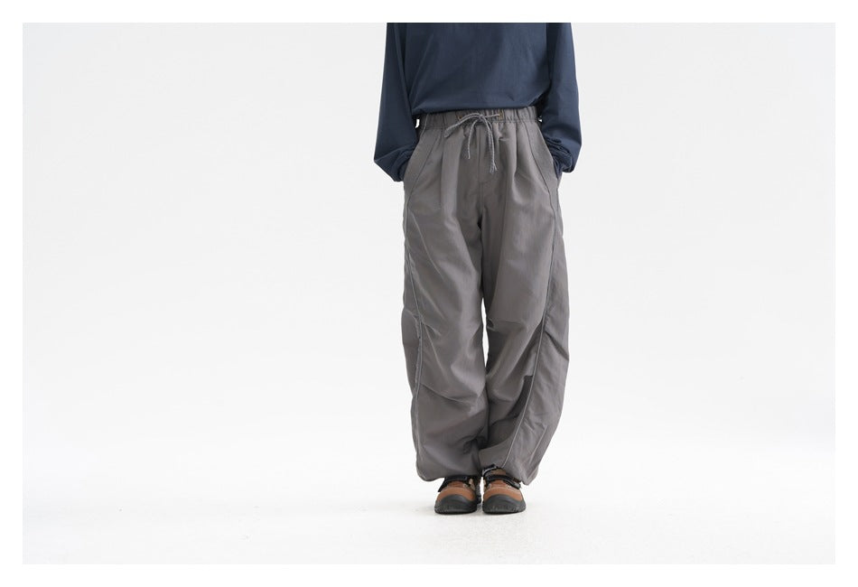 Front view of a model wearing loose gray drawstring pants with curved side piping.