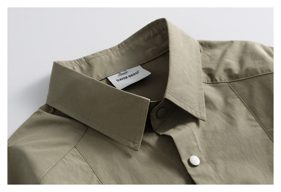 Close-up of an olive-khaki shirt collar, stitched seams, snap buttons and inner label.