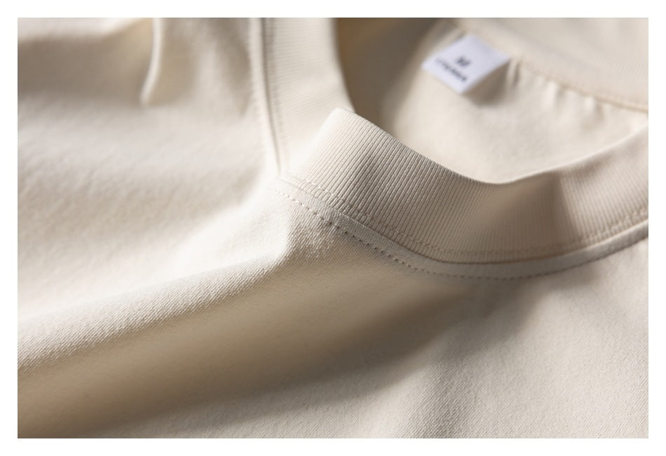 Close-up of the cream sweatshirt's ribbed crew neckline and stitching, with a small inner label.