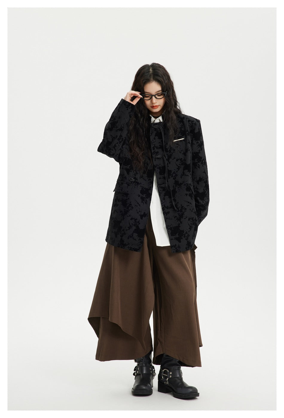 Full-length model wearing a black abstract-patterned toggle-front jacket, white shirt, brown draped wide-leg trousers and