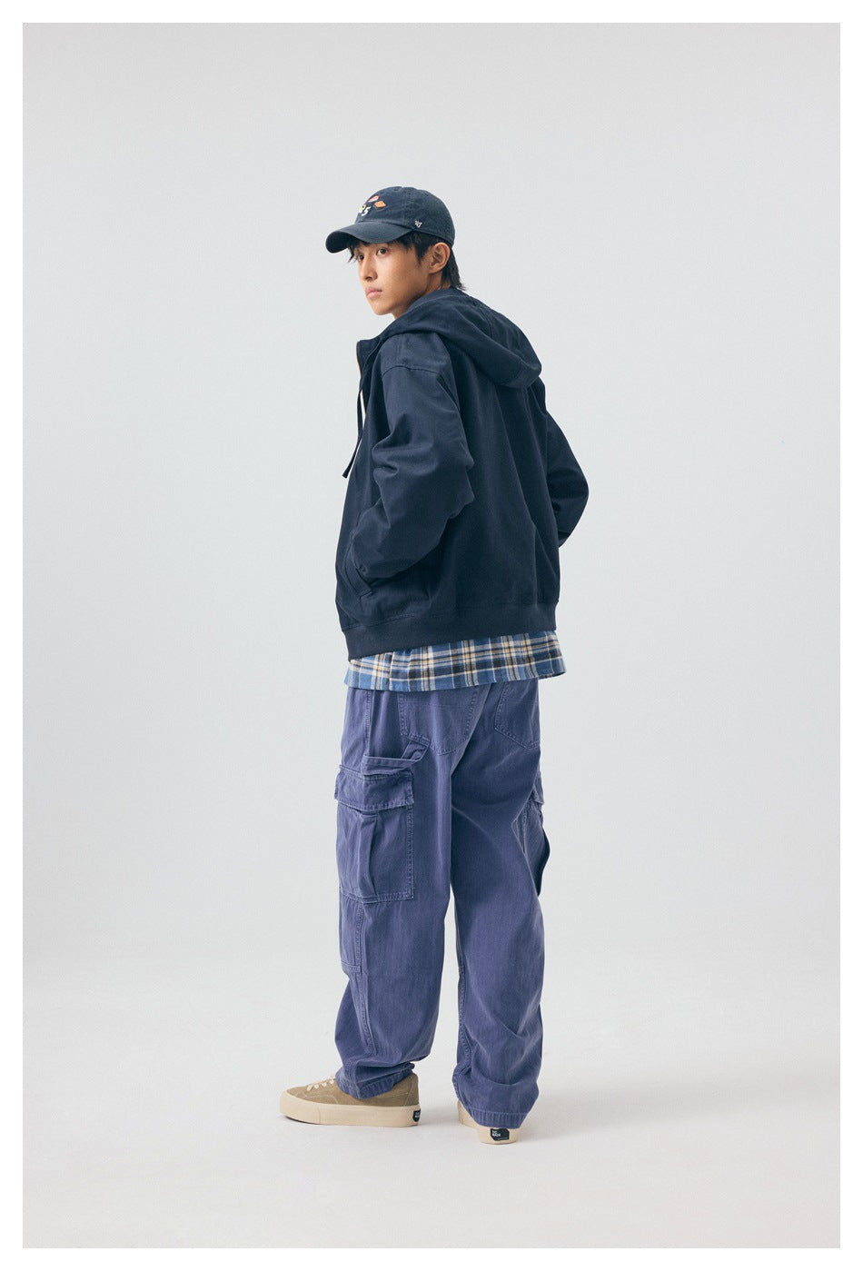 Model wearing navy hooded jacket over a plaid shirt, turned side-back view showing hood and ribbed hem