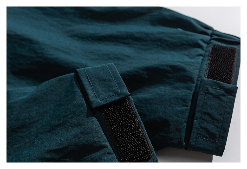 Dark teal garment detail showing black hook-and-loop fastening straps and stitched tabs.
