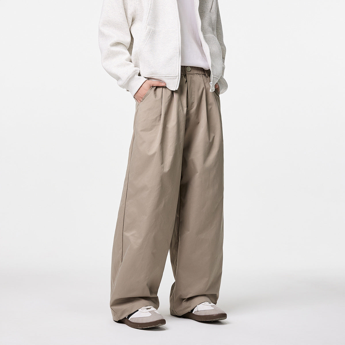 Angled view of a model wearing loose taupe trousers with a button waist and a light zip hoodie.
