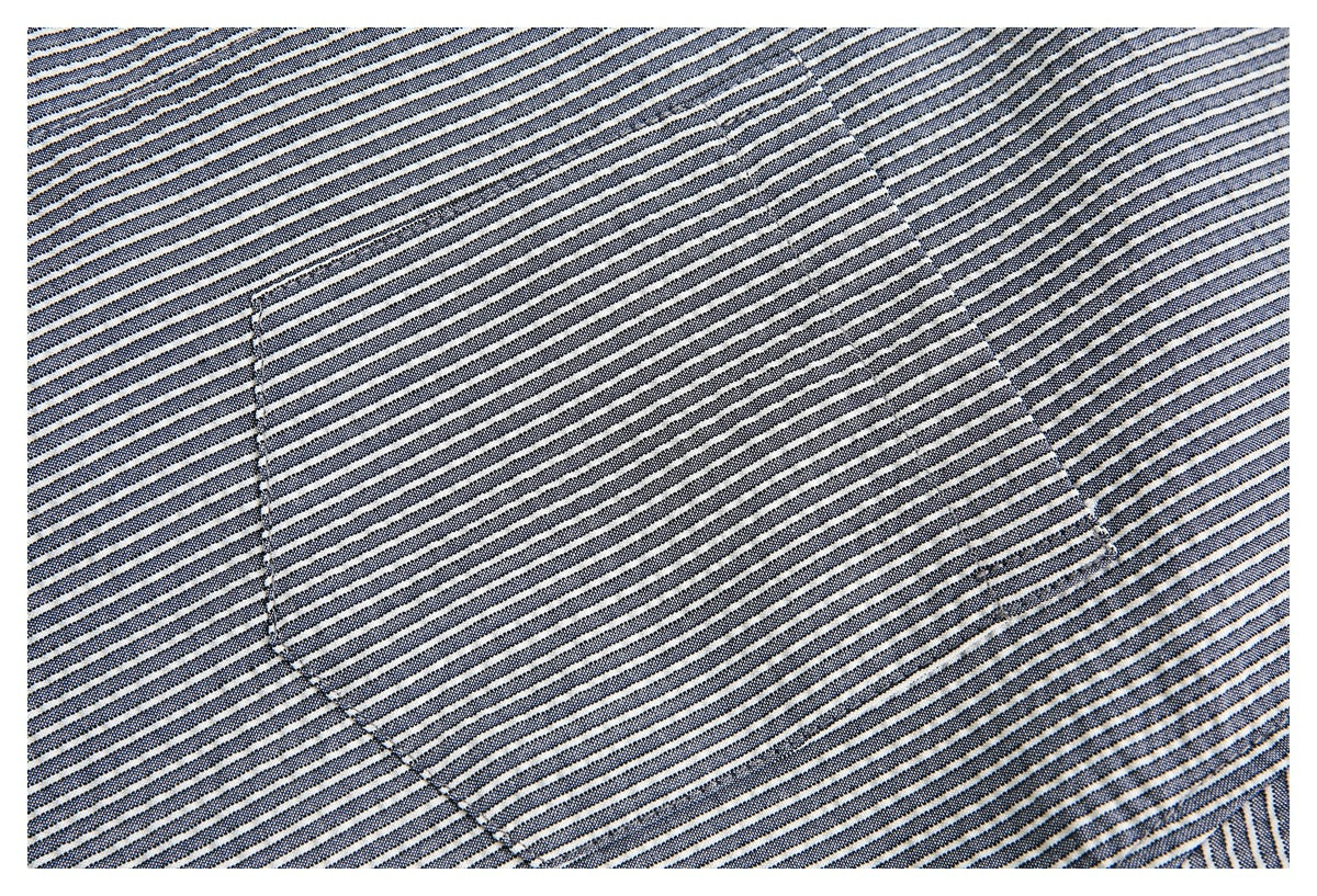 Close-up of a stitched chest pocket on dark fabric with narrow light stripes.