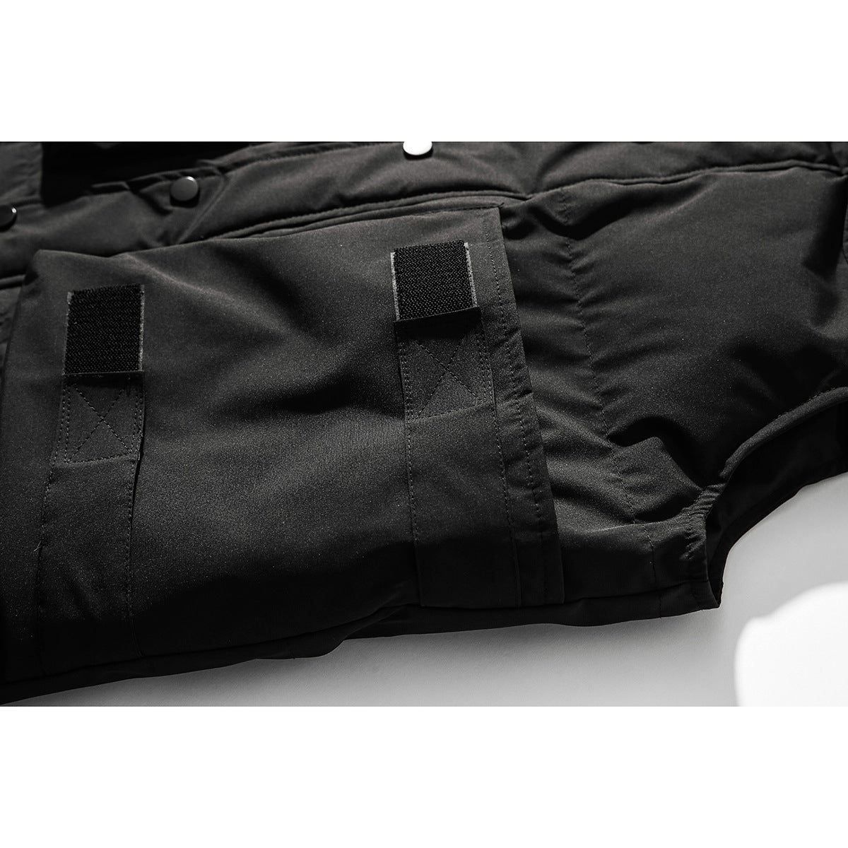 Close-up of a black jacket pocket with two vertical hook-and-loop fastening tabs.
