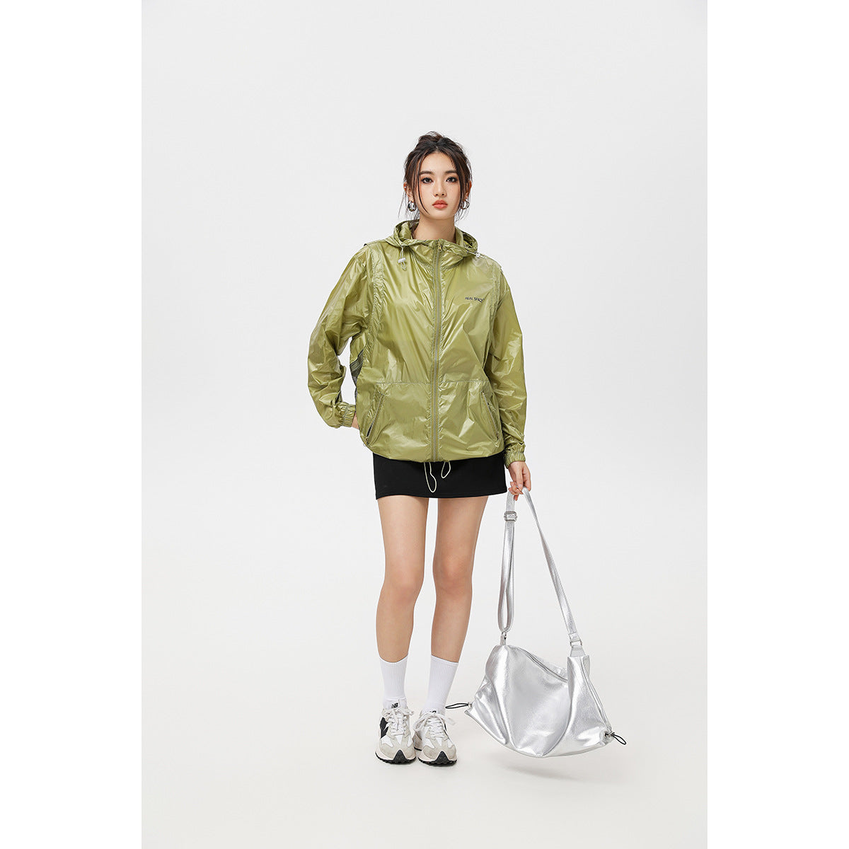 Model wearing a shiny olive-green hooded jacket with a front zip and drawcord hem, paired with a black skirt.