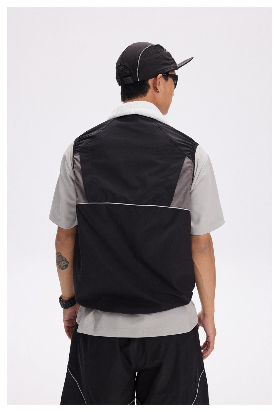 Back view of a model wearing a black vest with gray mesh side panels and thin white piping.