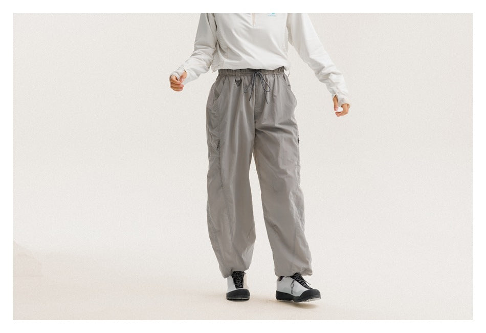 Cropped model wearing loose gray drawstring pants with slanted pockets and gathered ankles, shown from the front.