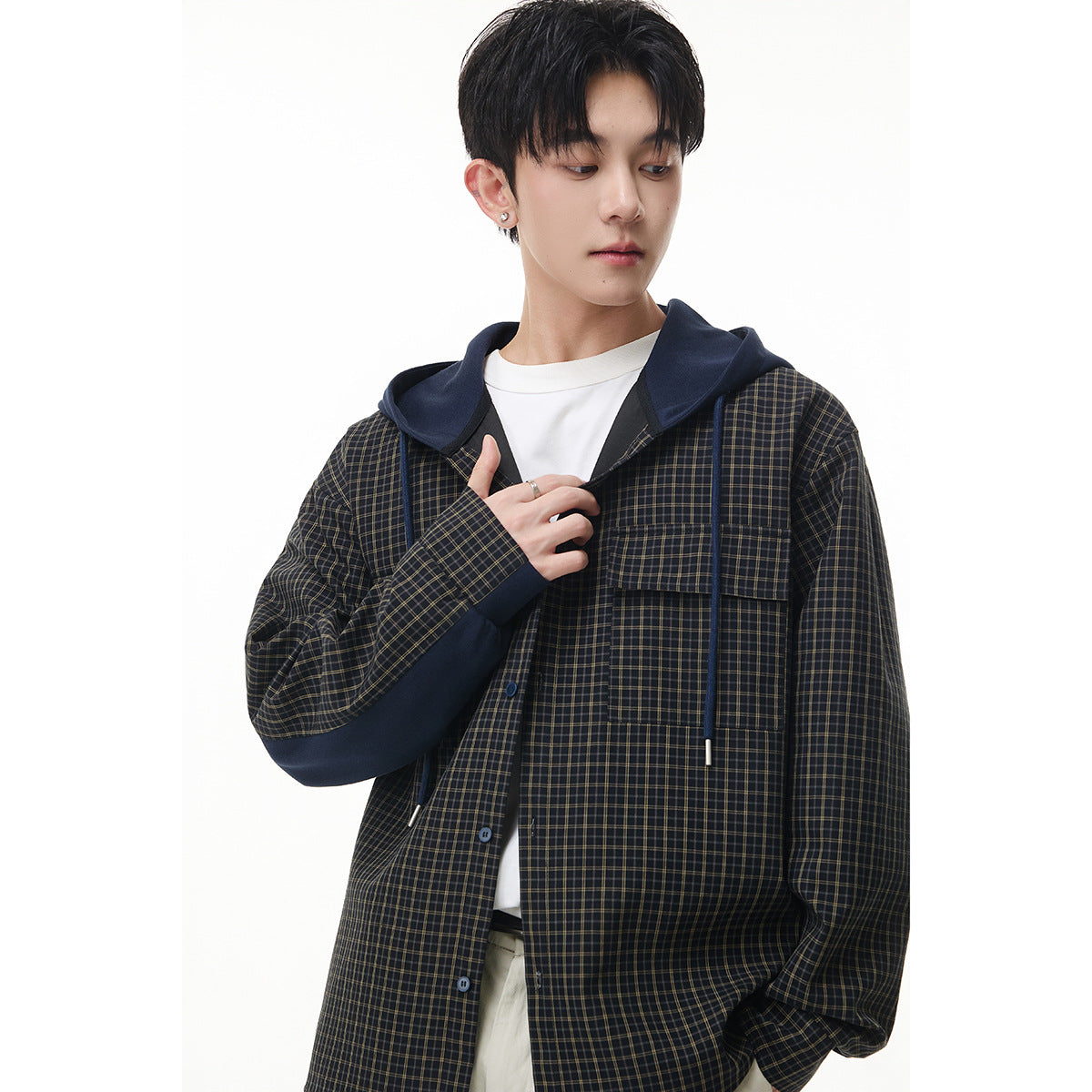Model in a close front view of a dark plaid button-up hooded jacket with navy hood, drawstrings, and large flap pockets.