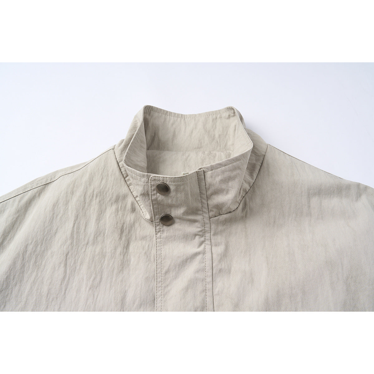 Close-up of a light gray-beige jacket's tall stand collar and two dark metal snap buttons.