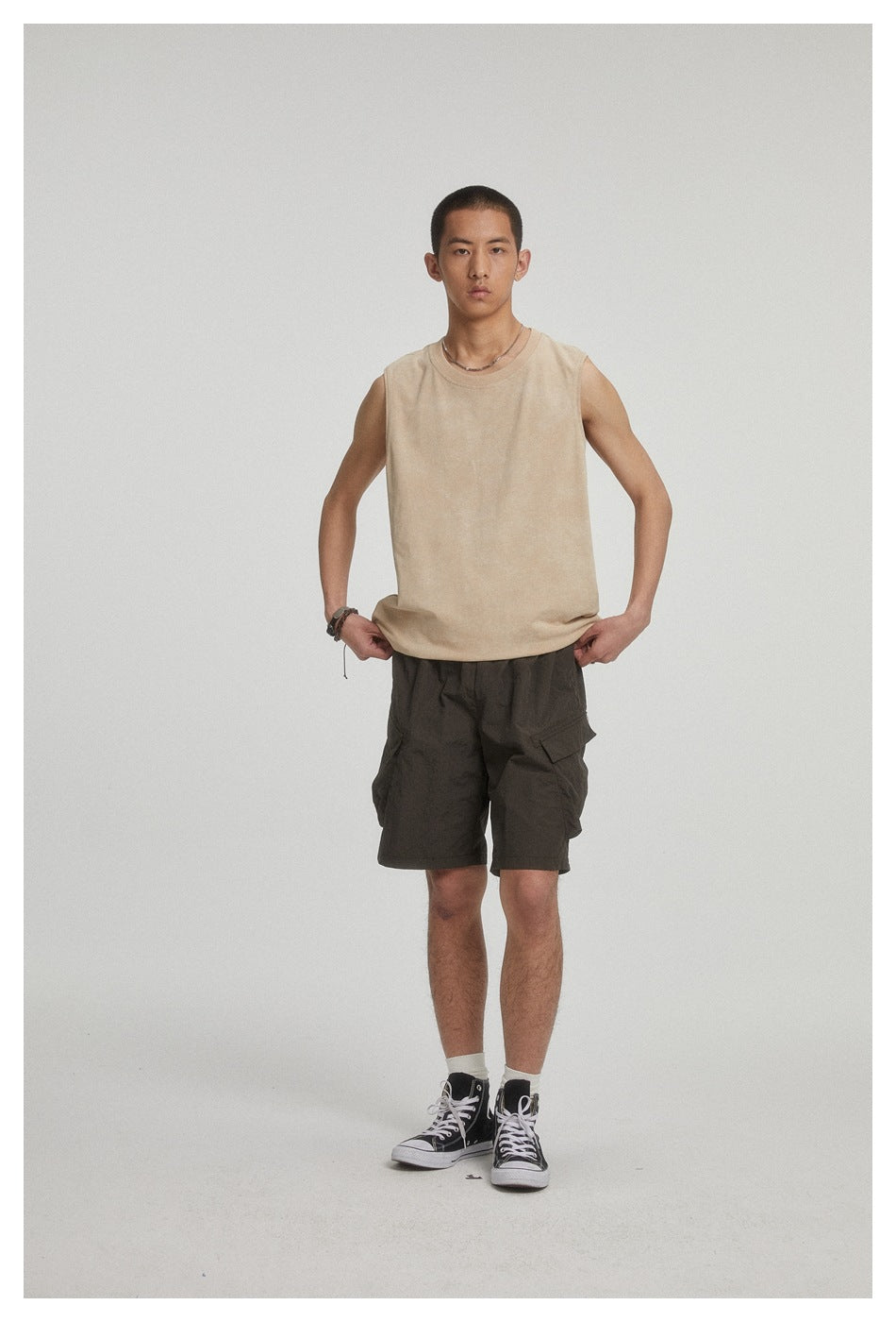 Front view of a man wearing a beige sleeveless top and dark cargo shorts.