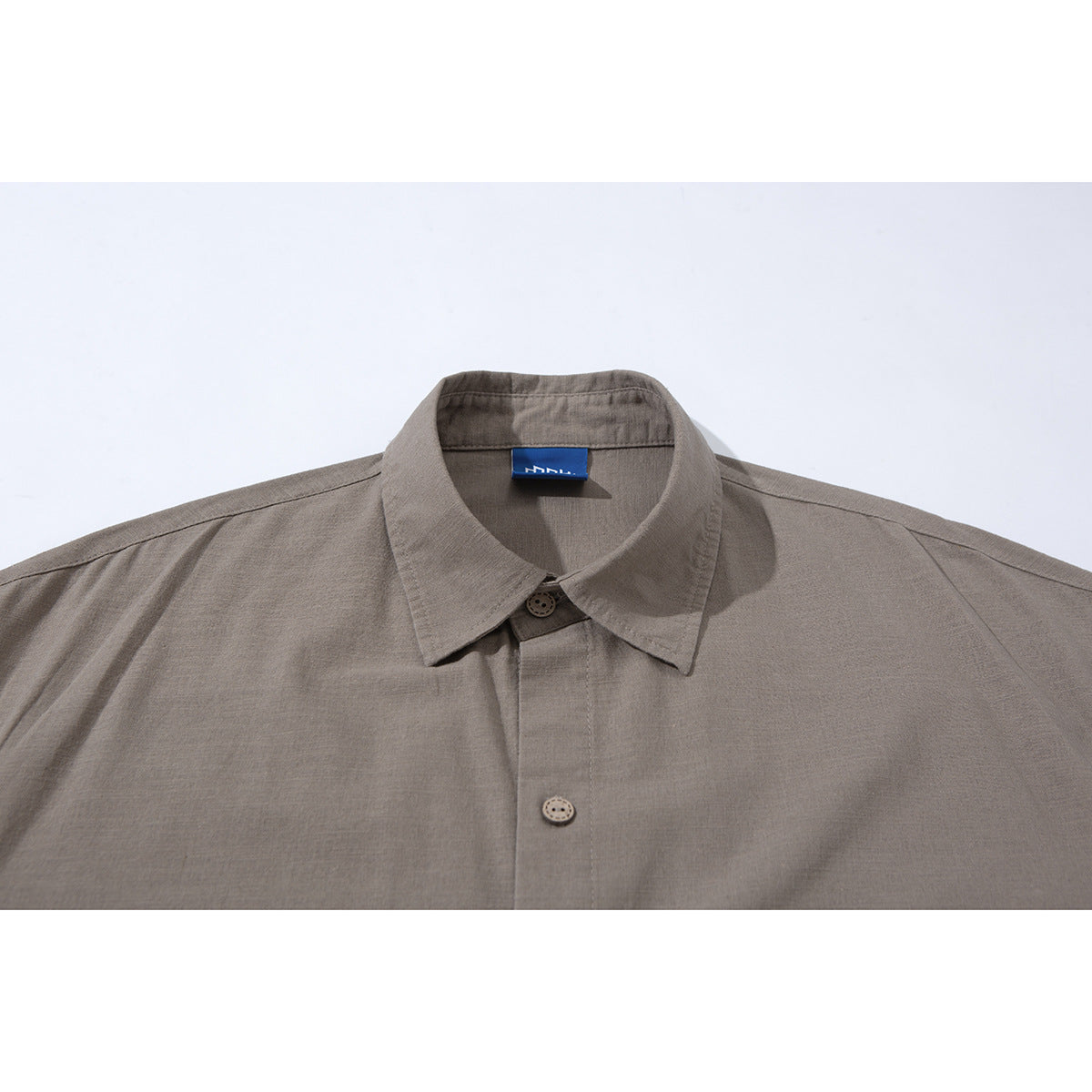 Close-up of a taupe short-sleeve shirt collar, button placket, and blue neck label.