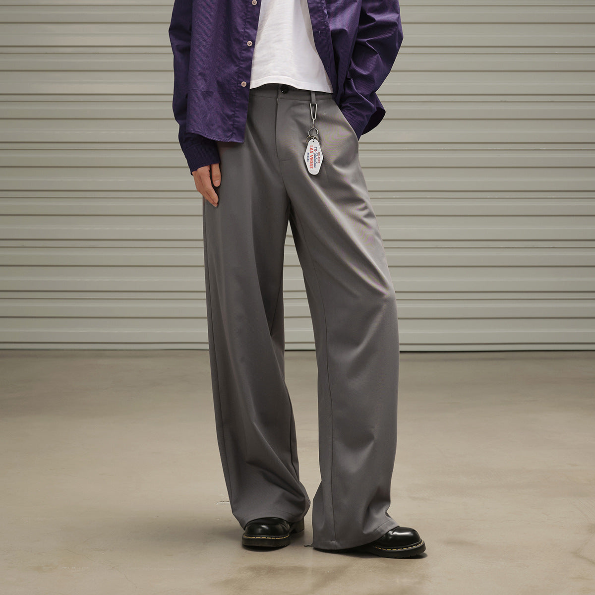 Close view of a model wearing wide gray trousers with a purple overshirt and a clipped tag.