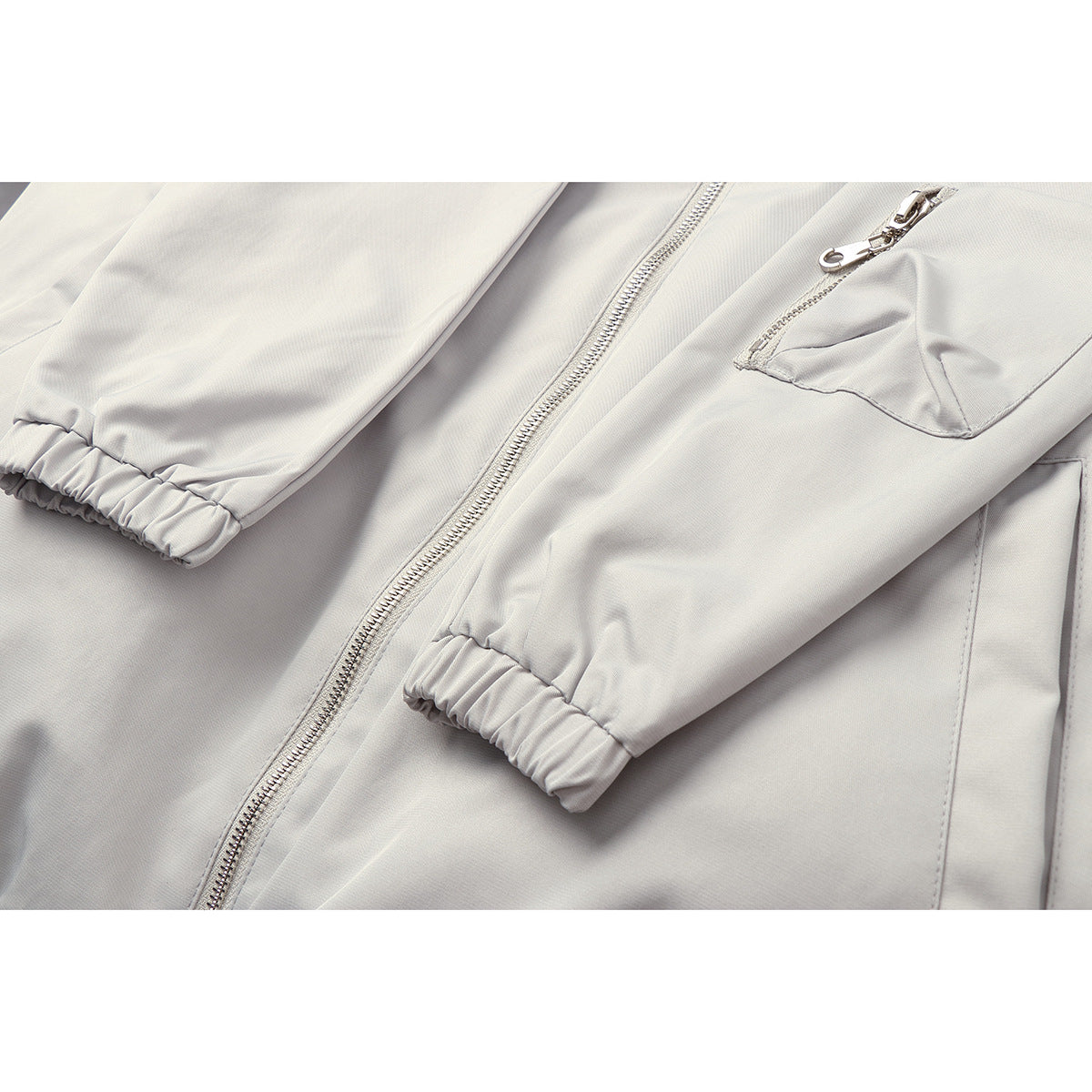 Pale gray jacket close-up showing the front zipper, zip pocket, sleeve, and elastic cuff.