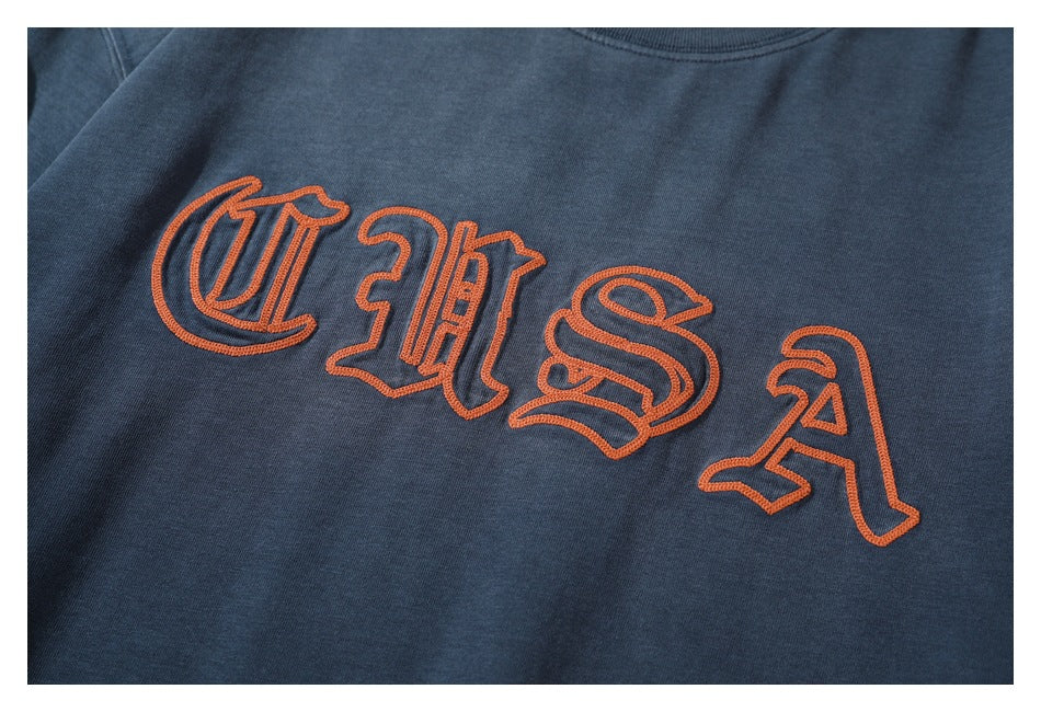 Close-up of orange outlined lettering embroidered across a dark navy shirt chest.