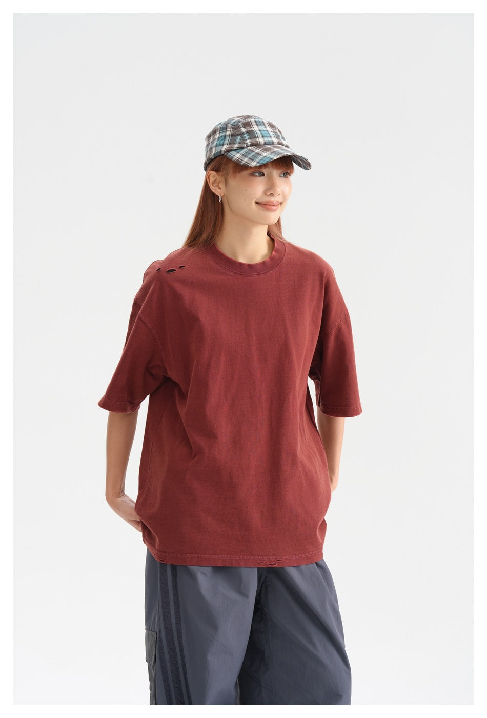 Closer view of a model wearing a brick-red oversized T-shirt with small shoulder holes and gray cargo pants.