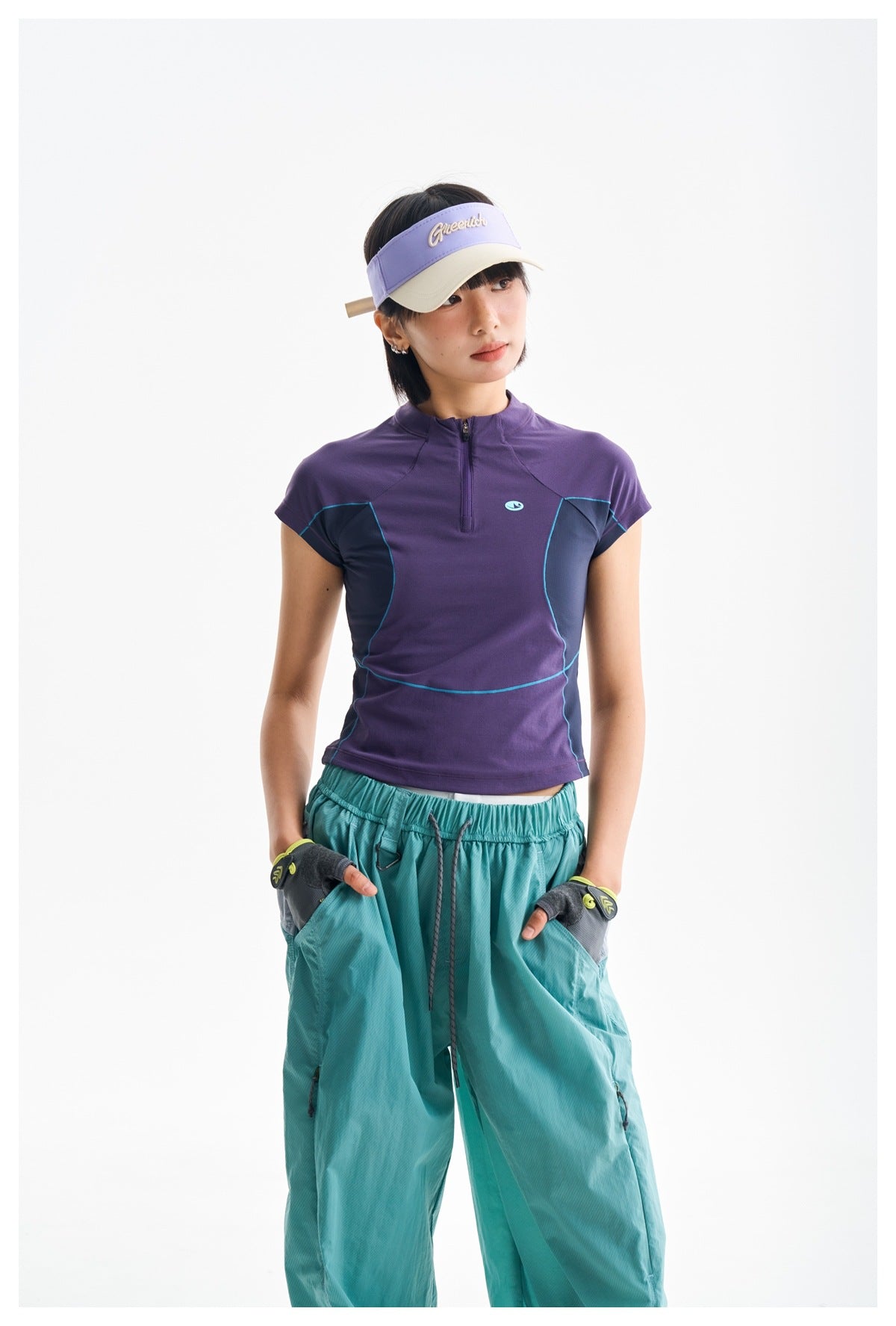 Front view of a model wearing a purple athletic top with dark side panels and teal piping, plus loose teal pants.