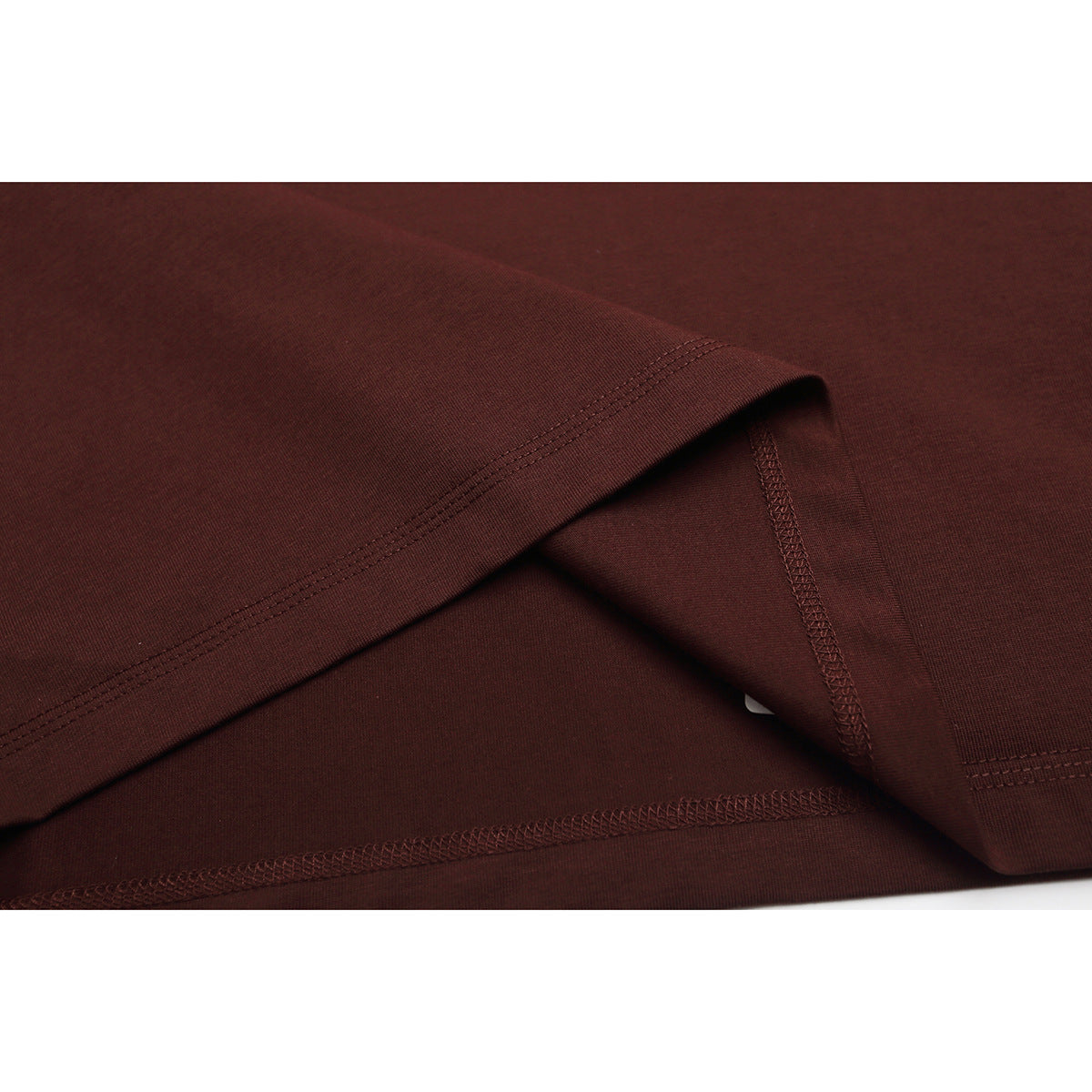 Close-up of the burgundy T-shirt's folded hem and overlocked seam stitching.