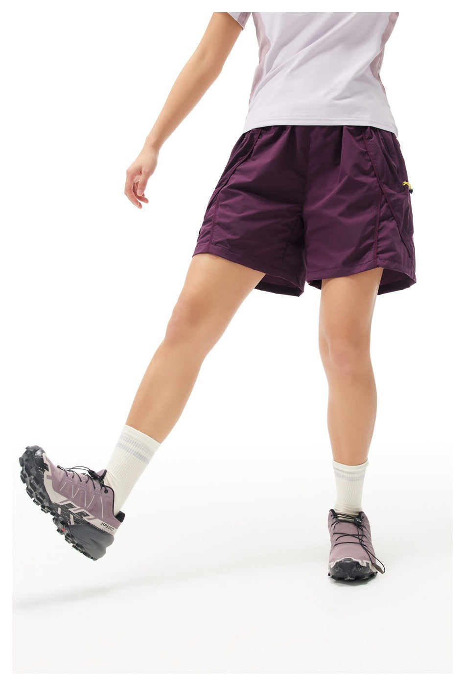 Front angled view of a model wearing plum athletic shorts with roomy legs and large side pockets.