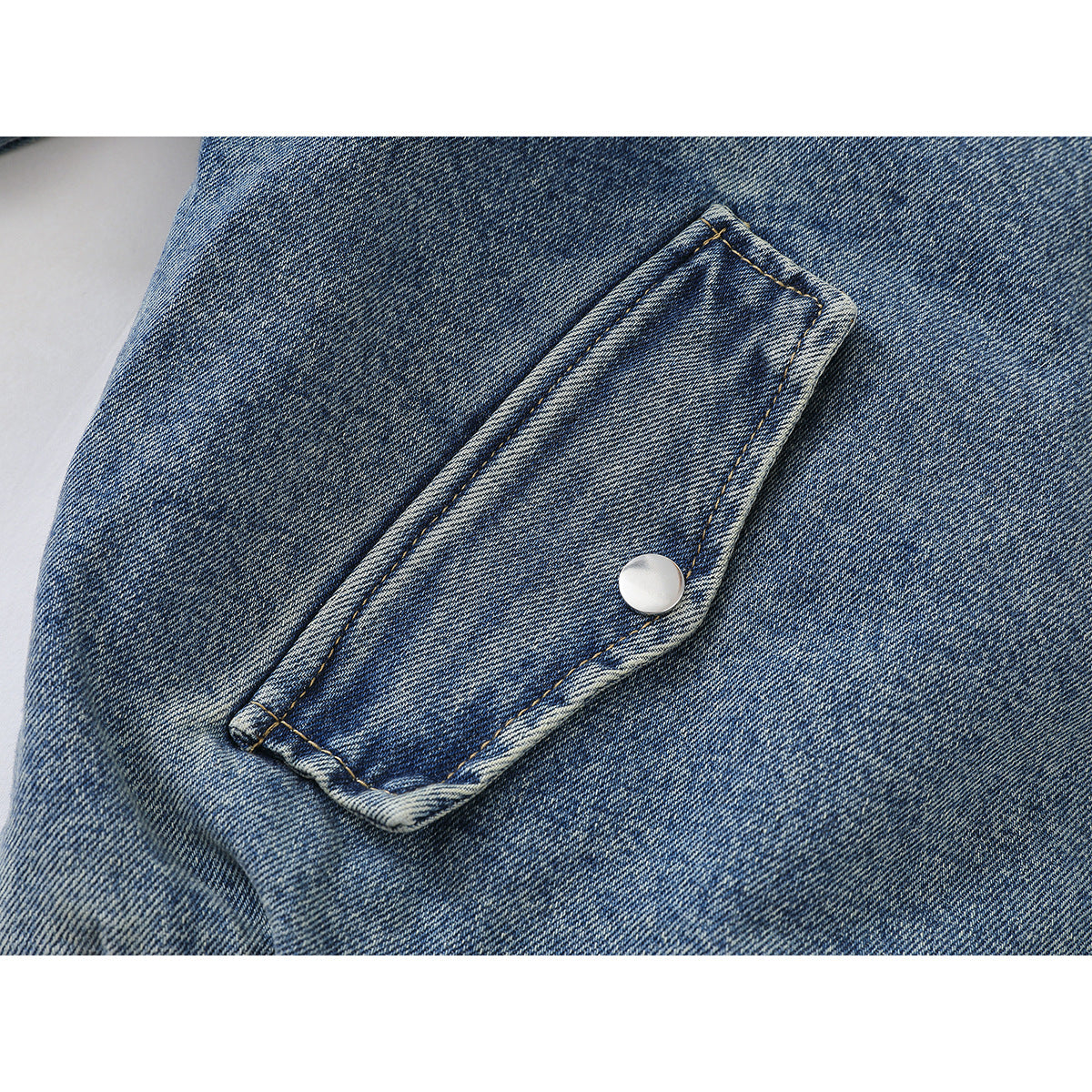 Close-up of a flap pocket with a silver snap on blue denim.