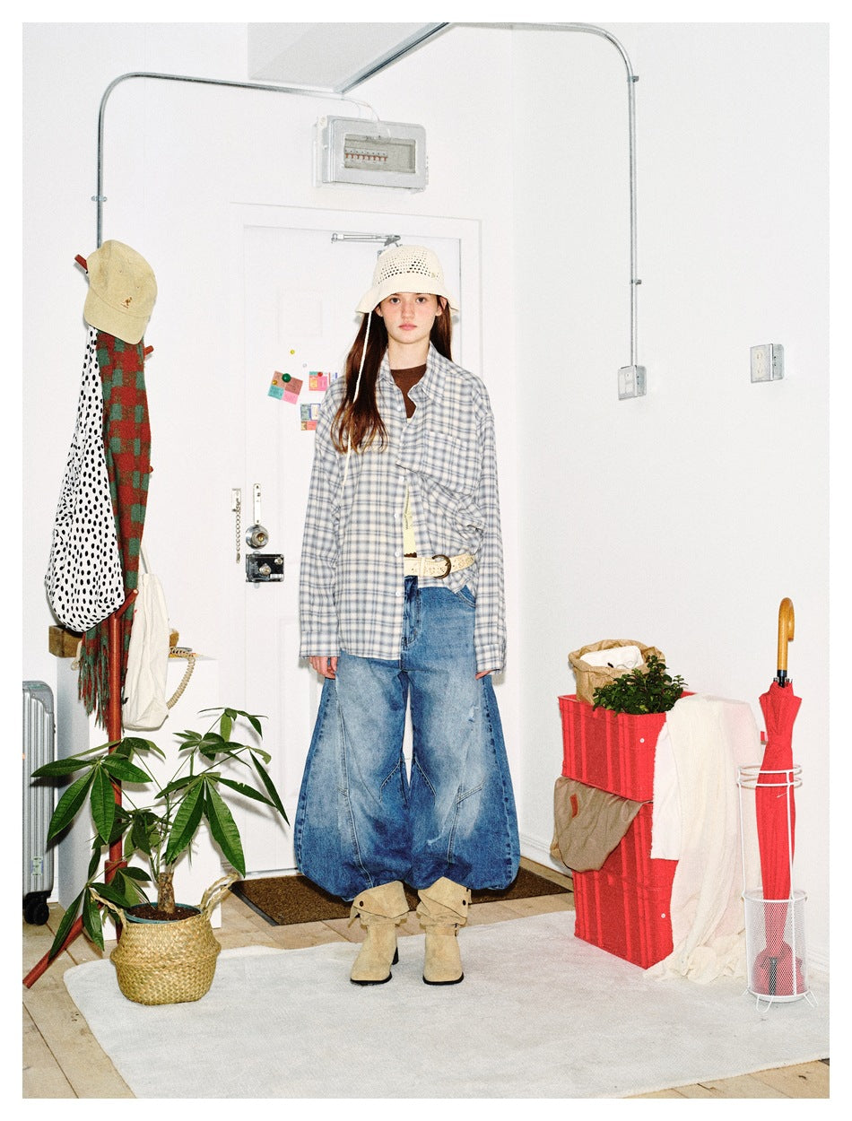 Model wearing an oversized light blue plaid shirt open over a brown top with wide-leg jeans, bucket hat and suede boots