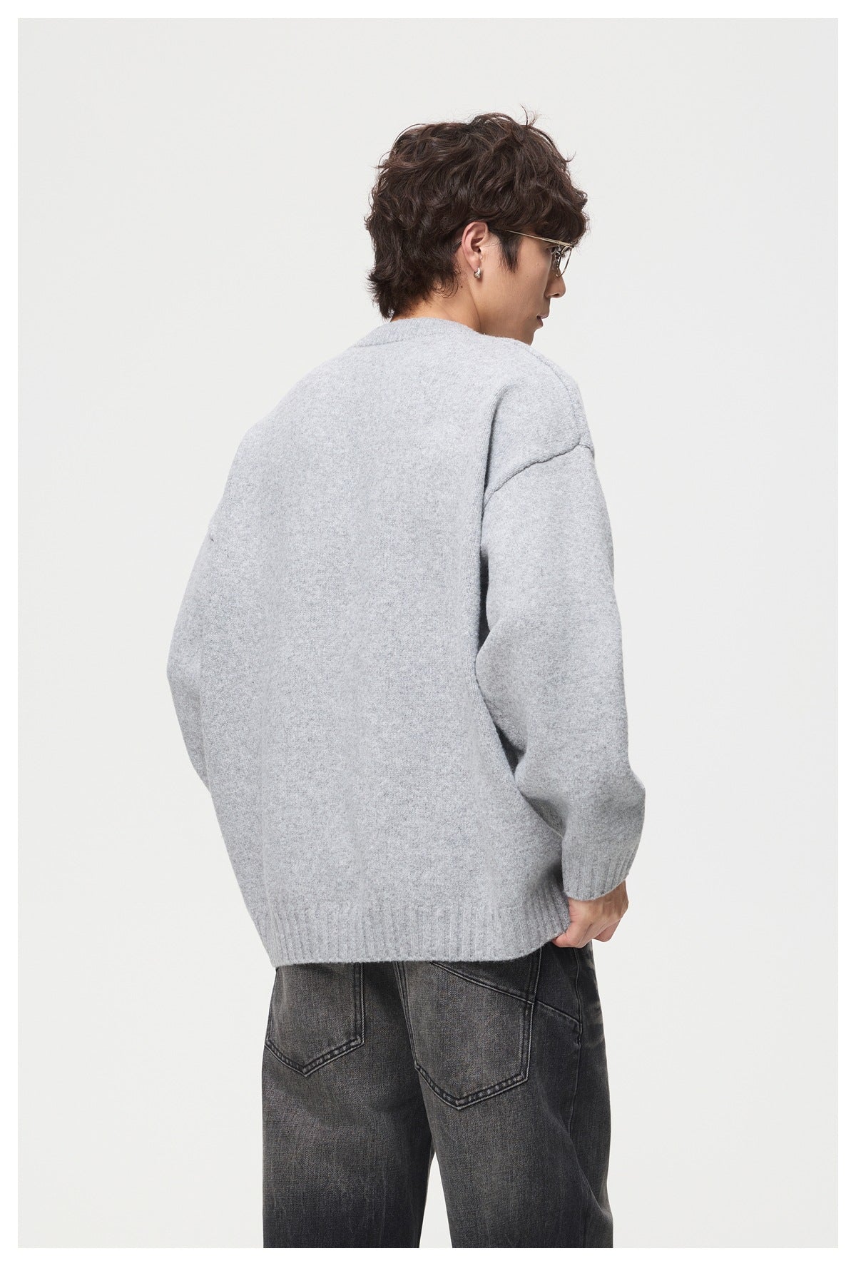 Back view of a model wearing a light gray sweater with a plain back, dropped shoulders, and ribbed hem and cuffs.