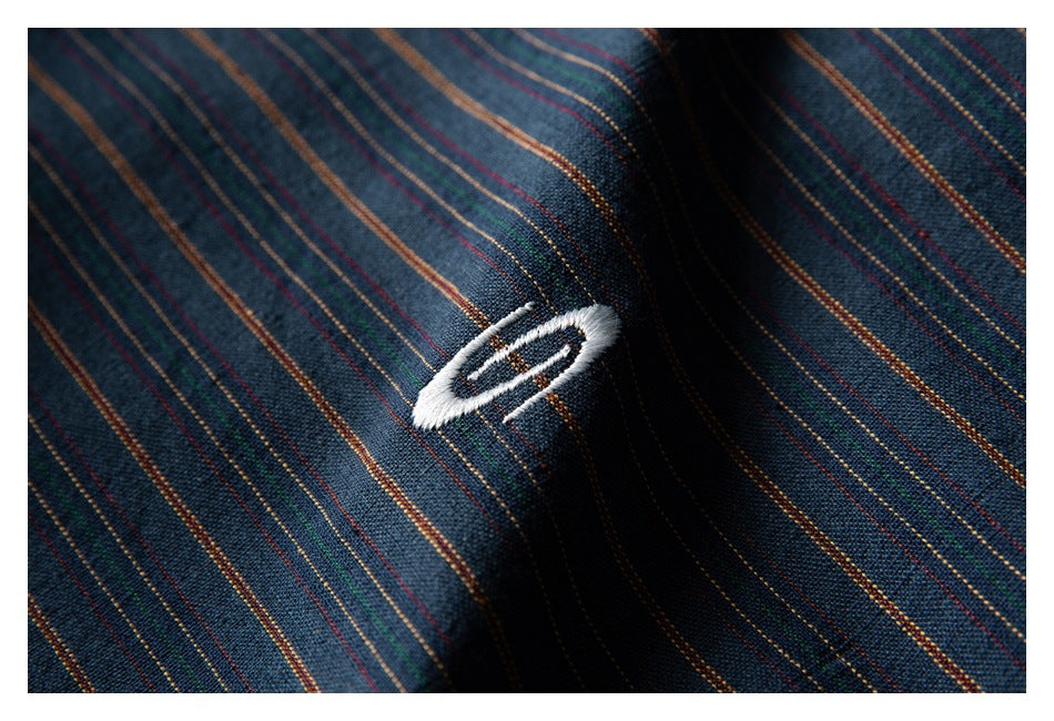 Close-up of a white embroidered oval mark on dark blue fabric with thin multicolor stripes.