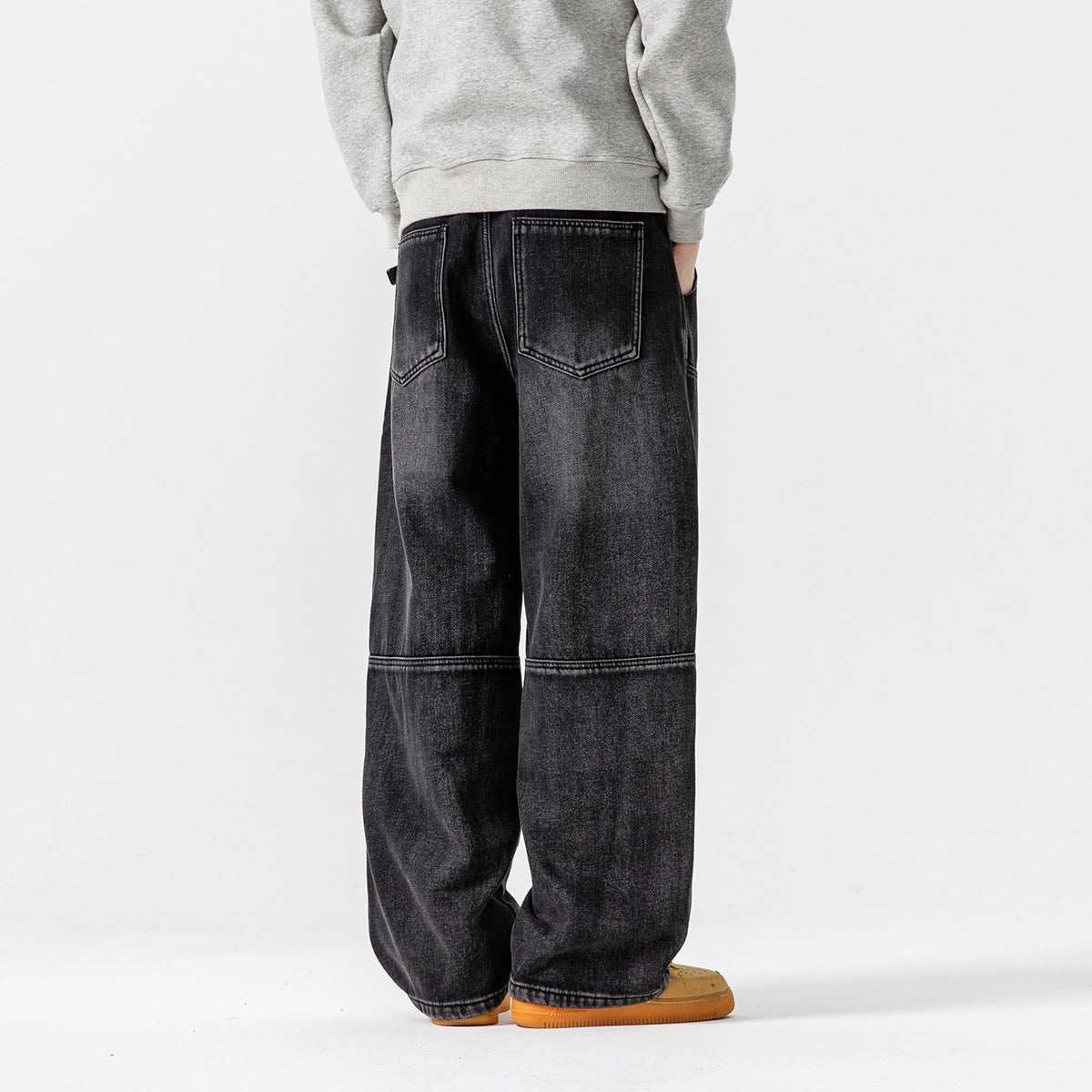Rear view of a model wearing loose black washed jeans with two back pockets and horizontal leg seams.