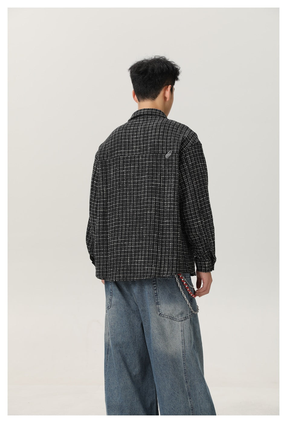 Back view of a model wearing a black grid-check shirt-jacket with a small paperclip embroidery and wide jeans