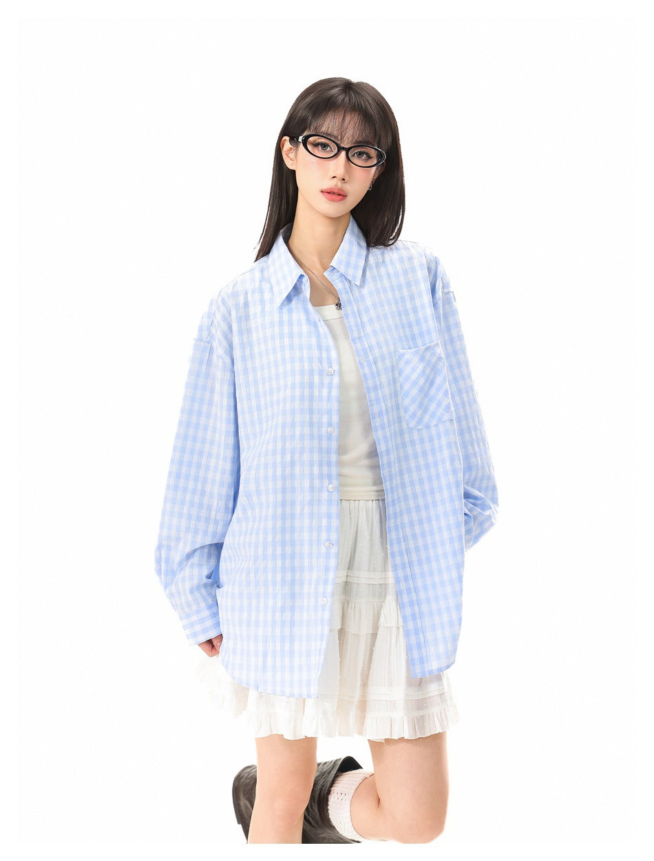 Model wearing an open light blue gingham oversized shirt over a white tank top and white tiered skirt