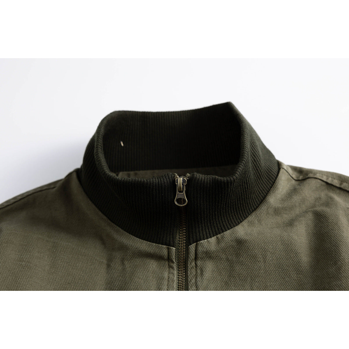 Close-up of an olive jacket’s dark ribbed stand collar and front zipper.