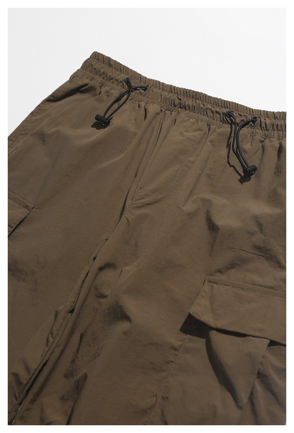 Close-up of brown cargo pants showing the elastic drawcord waist, front pocket, and cargo pocket flap.