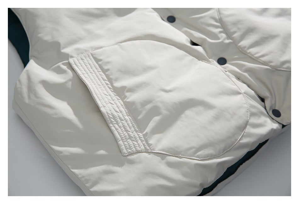 Close-up of a white garment with a rounded pocket, stitched trim, and dark snap buttons.