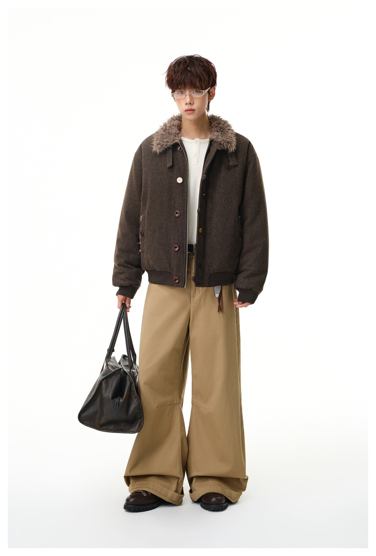 Model wearing a dark brown jacket with a plush collar, front zipper and buttons, paired with wide tan trousers and a black