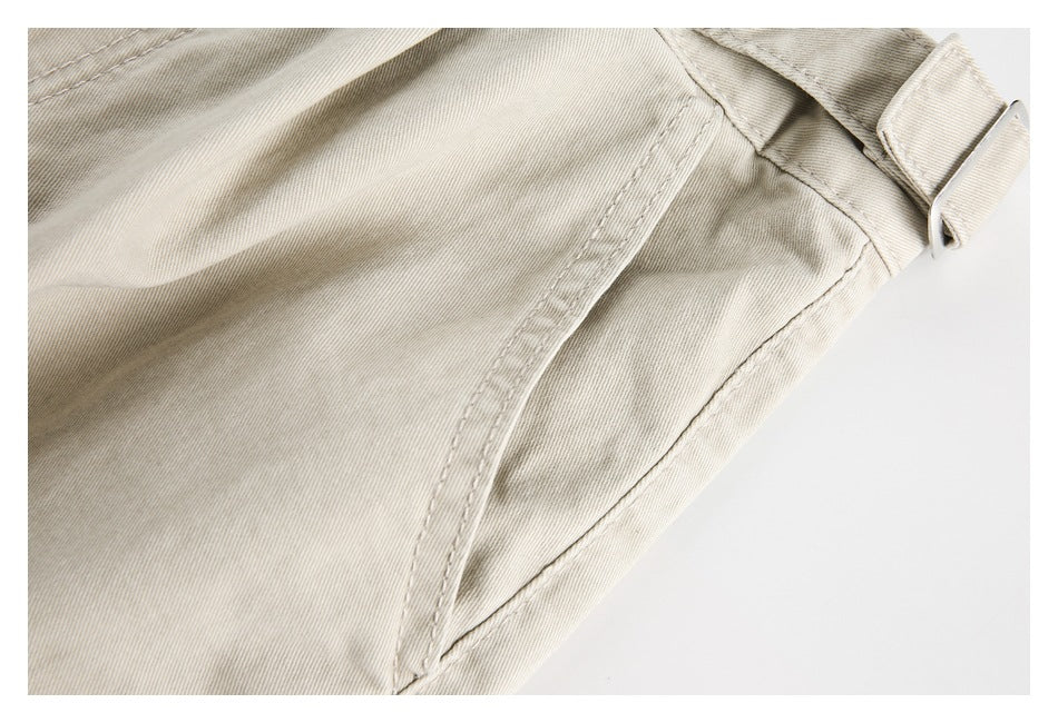 Close-up of the beige trousers' side seam and adjustable waistband tab with a metal buckle.