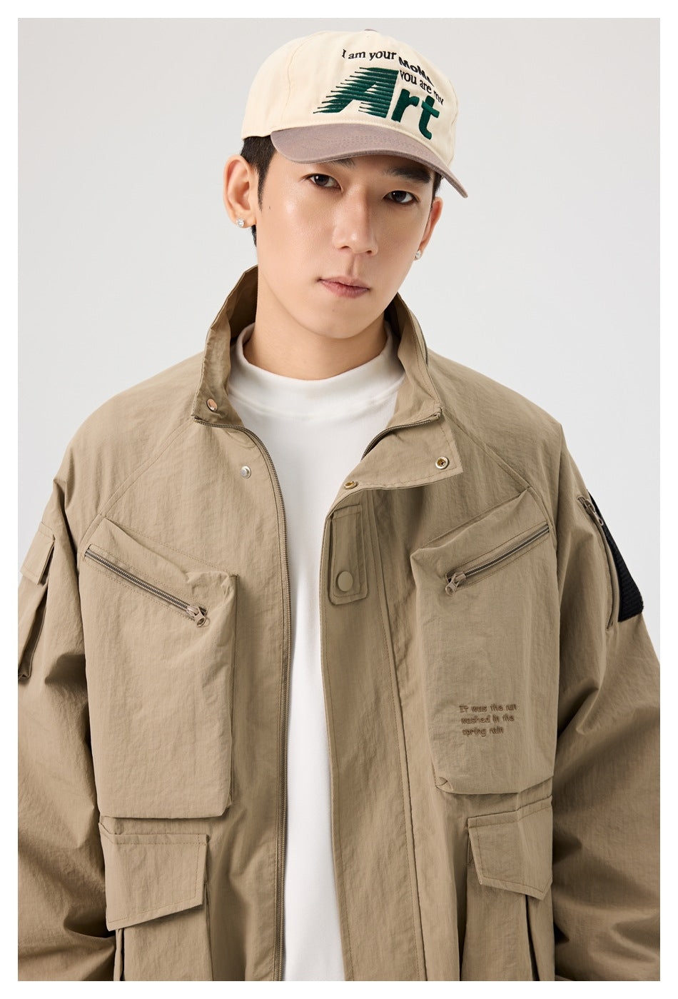 Close-up of a man wearing a khaki stand-collar jacket with zip chest pockets and embroidered chest text