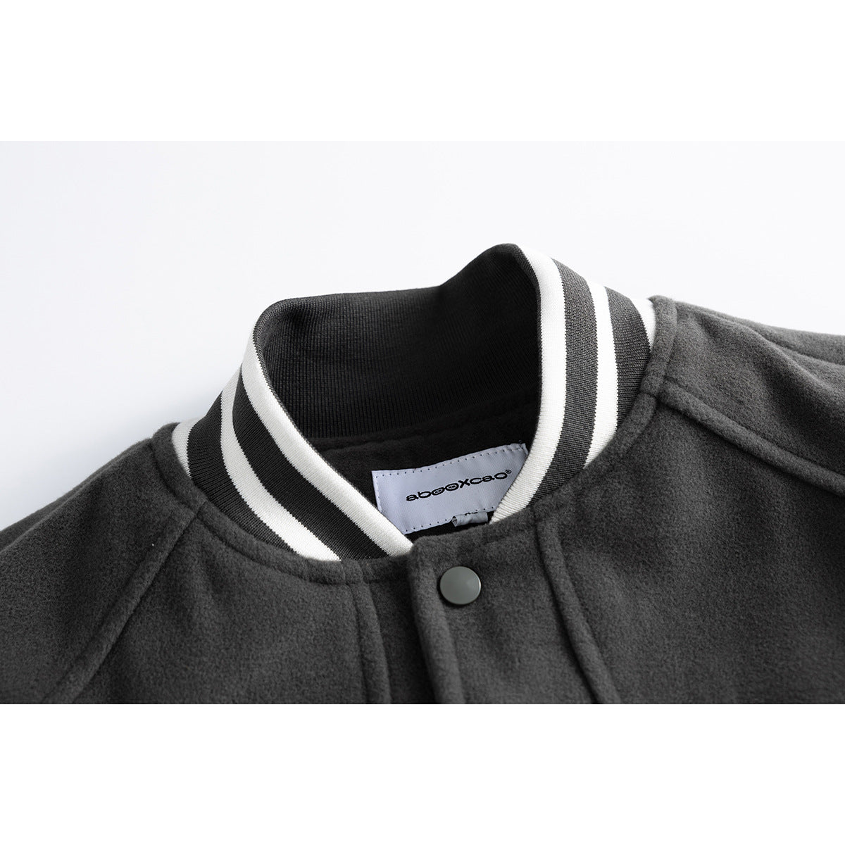 Close-up of a charcoal varsity jacket collar with black-and-white striped ribbing, a snap button, and an inner label.