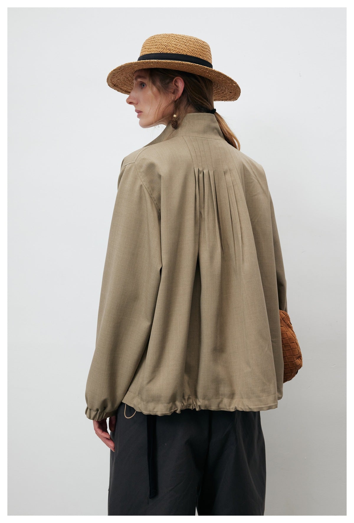 Model shown from behind wearing a taupe jacket with a pleated back and gathered hem.